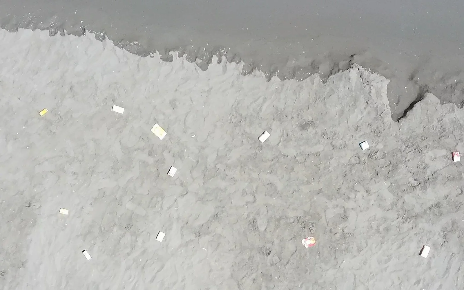Raw aerial frame of a shoreline, litter barely visible against wet sand